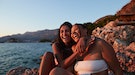 two women smile and embrace as they enjoy golden hour at the beach and consider the spiritual meanin...