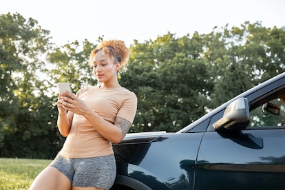 Young woman texting next to her car before hiking during the June 2023 full Strawberry Moon, which w...