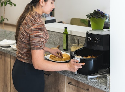 Teenage woman preparing fried chicken in a deep fryer pot in her home kitchen