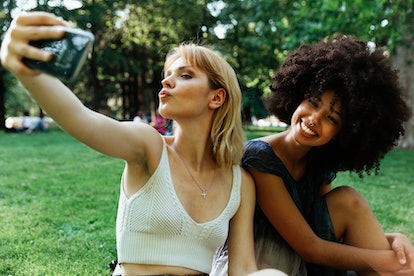 two women pose for a selfie together at the park as they consider how their zodiac signs are sociall...